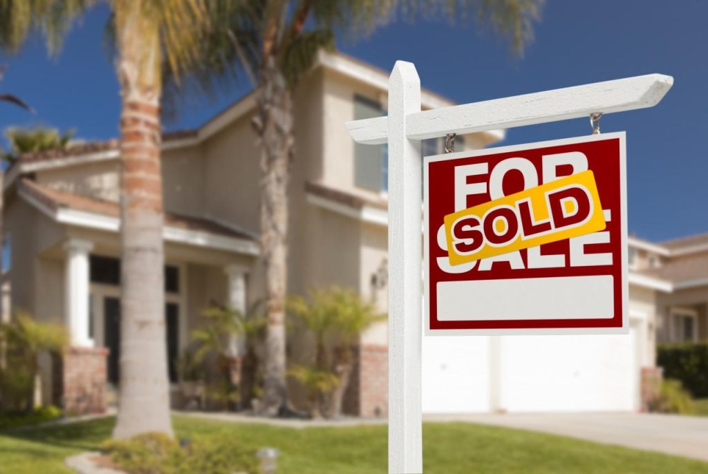 A red For Sale sign with a Sold rider in front of a suburban home